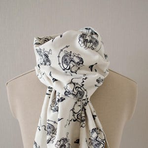 May include: A white scarf with a black and white print of Japanese mythical creatures. The scarf has a fringed edge.