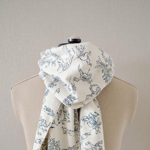 May include: A white scarf with a blue and white pattern of stylized animals and plants. The scarf has a frayed edge.