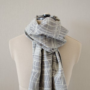 May include: A gray scarf with a white geometric pattern. The scarf is folded and draped over a mannequin.