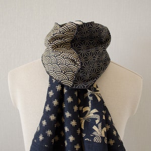 Op de afbeelding: Een patroon sjaal in marineblauw en beige, weergegeven op een mannequin. De sjaal toont Japanse geïnspireerde ontwerpen zoals golven, geometrische vormen en kruispatronen. De sjaal heeft een gefranjerde rand.