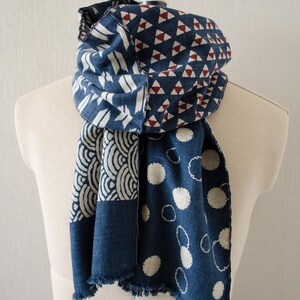May include: A blue scarf with various patterns, including white shapes and red triangles. The scarf is draped over a mannequin, showcasing its design and texture. The scarf has a fringed edge.