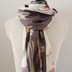 May include: A brown and cream-colored scarf with floral and striped patterns. The scarf is draped over a mannequin, showcasing its design. The scarf features a mix of colors, including brown, cream, blue, orange, and purple, creating a visually appealing accessory.