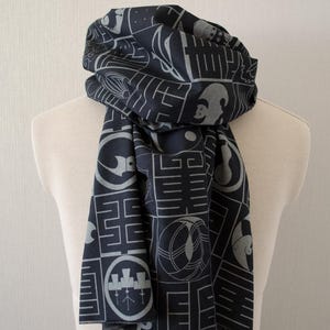 May include: A dark navy scarf with a repeating geometric pattern in light gray. The scarf is draped over a mannequin and features various shapes and symbols, creating a unique accessory.