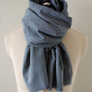 May include: A blue and white striped scarf draped over a mannequin. The scarf is made of a soft fabric and features thin, vertical stripes. The scarf is wrapped around the mannequin's neck and hangs down in soft folds.