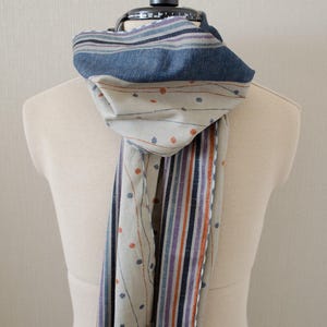 May include: A scarf with a blue, white, and orange striped pattern on one side and a white background with orange dots and thin lines on the other side.