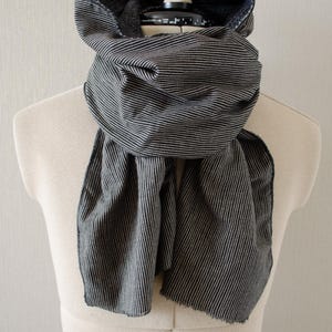 May include: A black and white striped scarf draped over a mannequin. The scarf is made of a soft fabric and features vertical stripes. The scarf is wrapped around the neck and drapes down the front.