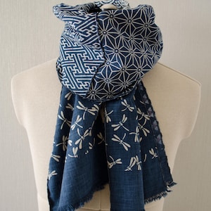 May include: A blue and white patterned scarf displayed on a mannequin. The scarf features geometric and dragonfly designs. The scarf is made of a soft fabric and has a fringed edge. The scarf is approximately 60 inches long.