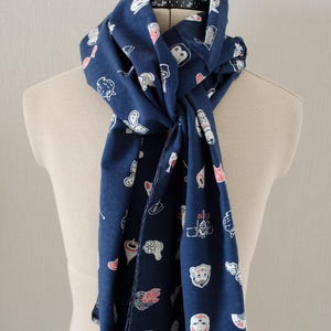 May include: A navy blue scarf with a white and red pattern of Japanese characters and symbols. The scarf is folded and tied around a mannequin's neck.