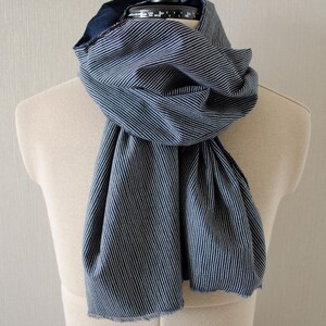 May include: A blue and white striped scarf draped over a mannequin. The scarf is made of a soft fabric and has a fringed edge. The scarf is wrapped around the mannequin's neck and hangs down the front.