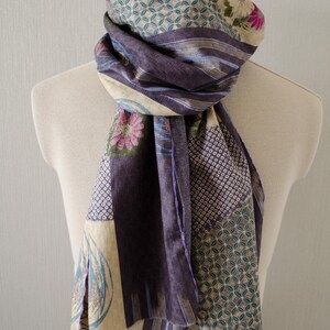 Könnte beinhalten: Ein rechteckiger Schal mit einem Patchwork-Design aus verschiedenen Stoffen in Violett-, Creme- und Petroltönen. Der Schal zeigt sich wiederholende geometrische Muster, florale Motive und gestreifte Abschnitte mit sichtbaren Nähten an den Kanten.