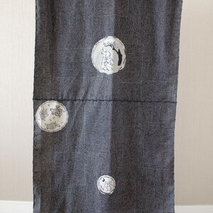 May include: Dark gray fabric with a vertical striped pattern and rectangular blocks. The fabric is decorated with several circular illustrations of rabbits and trees in white and black. The fabric is hanging.