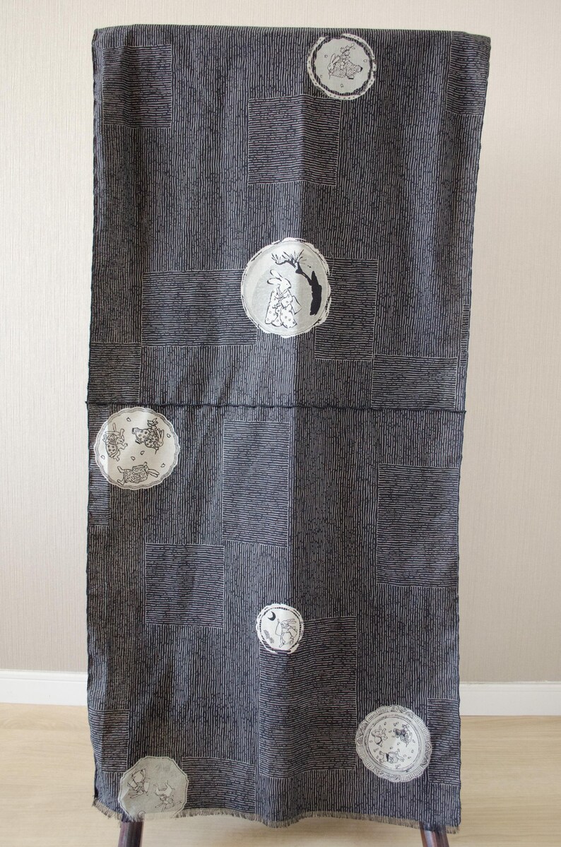 May include: Dark gray fabric with a vertical striped pattern and rectangular blocks. The fabric is decorated with several circular illustrations of rabbits and trees in white and black. The fabric is hanging.