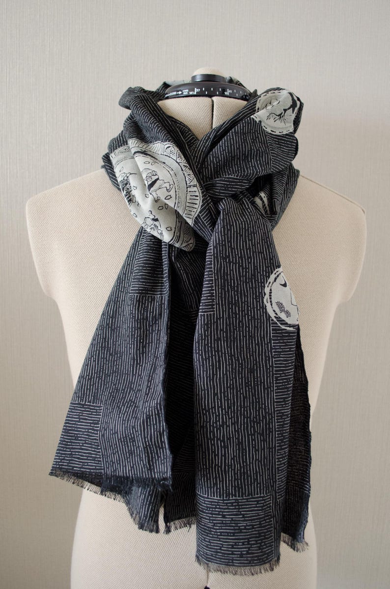 May include: A dark blue scarf with a white vertical stripe pattern and white circular designs. The scarf is draped over a mannequin, showcasing its length and design. The scarf has a fringed edge.