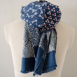 May include: A blue and white patterned scarf with a variety of designs, including dragonflies, geometric shapes, and wave patterns. The scarf is draped over a mannequin and has a fringed edge.