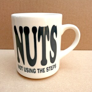 May include: White ceramic mug with black lettering that reads "NUTS NOT USING THE STEPS".