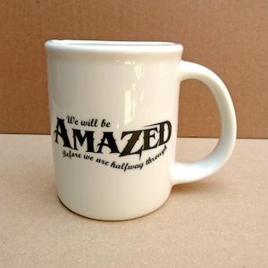 May include: White ceramic coffee mug with a black graphic that reads "We will be AMAZED Before we are halfway through".