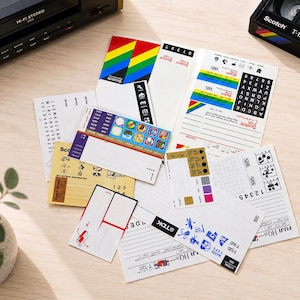 May include: A collection of assorted vintage VHS cassette adhesive labels featuring various brands like Scotch, TDK, and Fuji. The labels include colorful graphic designs, blank lines for writing, alphabet letters, and numbers for indexing tapes.