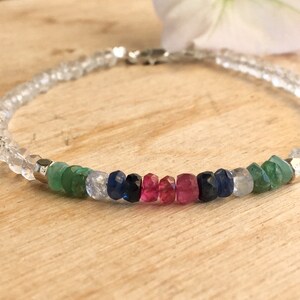 May include: A delicate bracelet with clear faceted beads and a colorful row of gemstones. The gemstones are green, blue, and pink.