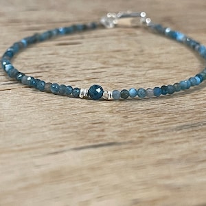 Peut inclure: Un bracelet délicat en pierres bleues avec un fermoir argenté. Le bracelet est composé de petites perles rondes et présente une pierre précieuse facetée plus grande au centre.