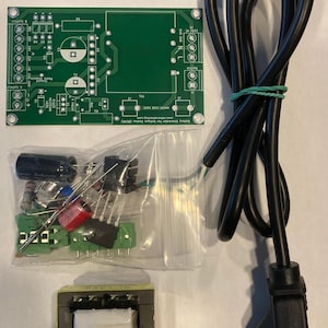 May include: A green circuit board with components, a transformer, a bag of electronic parts, and a black power cord with a plug.
