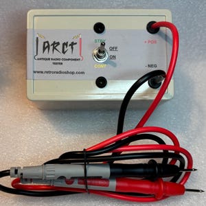 Könnte beinhalten: Eine weiße Box mit dem Text "I.A.R.C.T. Antique Radio Component Tester www.retroradioshop.com" und einem roten und schwarzen Kabel mit angeschlossenen Sonden. Die Box hat einen Schalter mit der Aufschrift "STBY OFF ON CONT" und zwei Buchsen mit der Aufschrift "POS" und "NEG".