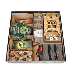 May include: A wooden board game organiser insert featuring laser-cut compartments for cards, tokens, and miniatures. The box includes a castle-themed structure, four white six-sided dice, and various game components organised in slots. The Tower Rex logo is visible.