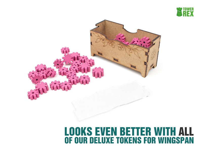 May include: A rectangular wooden storage box with laser-etched floral details, containing several small, bright pink, gear-shaped tokens. Additional pink gear-shaped tokens are scattered on the surface next to the box, alongside a blank white rectangular card.