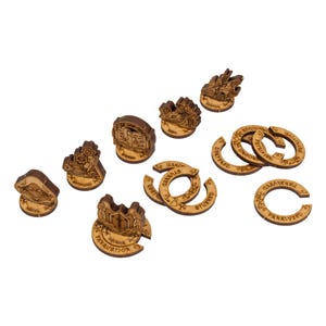 May include: A collection of laser-cut wooden game pieces, including various shapes and sizes. Some pieces are circular with text, while others are shaped like buildings or shields. The pieces are light brown with engraved details.