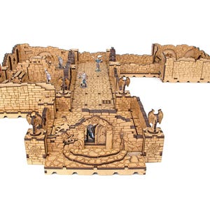 May include: A modular tabletop dungeon terrain set constructed from light brown laser-cut wood. The structure features interlocking stone-patterned walls, a central corridor, arched doorways, and decorative pillars topped with winged gargoyle figures.