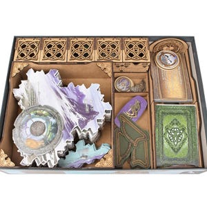 May include: A wooden board game organizer insert featuring laser-cut compartments with intricate knotwork patterns. The tray holds stacks of irregular shaped game tiles, decks of cards with green and gold backs, and various circular tokens.