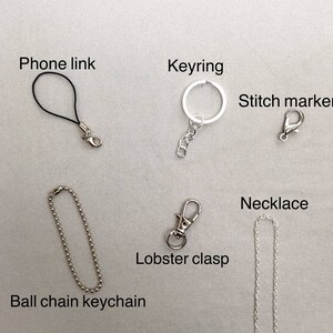 May include: Assortment of silver-toned metal clasps and chains, including a phone link, keyring, stitch marker, ball chain keychain, lobster clasp, and necklace.