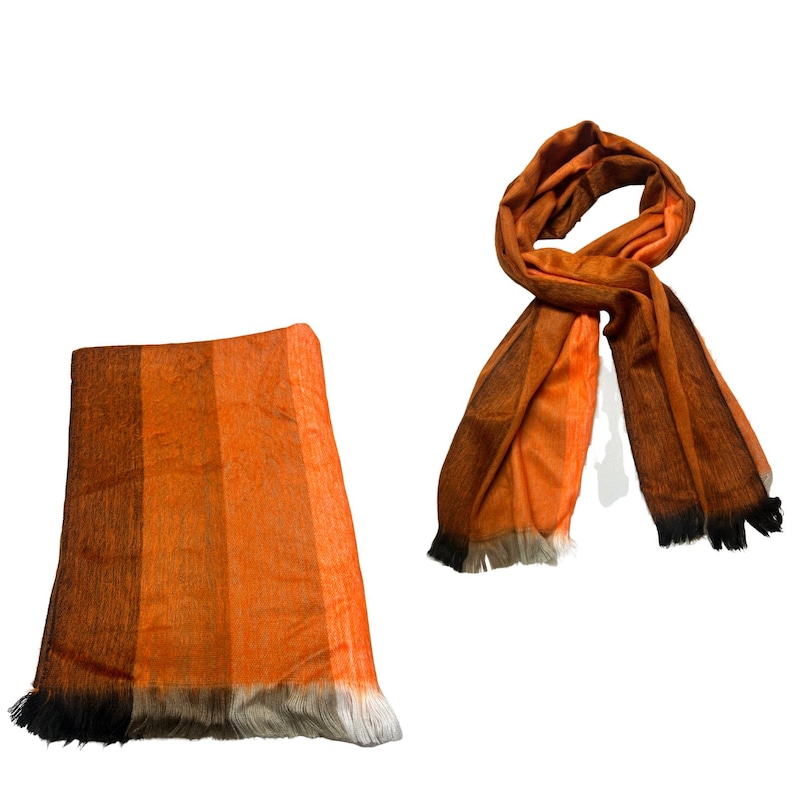 May include: A rectangular scarf featuring a gradient of orange, brown, and black tones with a fringed edge, displayed both folded in a flat, vertical orientation and loosely draped in a circular, knotted configuration against a white background.