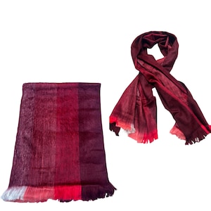 May include: Two burgundy scarves. One is folded, showing a gradient of colors from dark purple to red, with a fringed edge. The other is draped, displaying a similar color scheme, with fringed ends. Both scarves are made of a soft, woven material.
