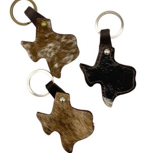 May include: Three leather keychains shaped like the state of Texas. One keychain is brown with white spots, one is black with white spots, and one is brown with white and black spots.