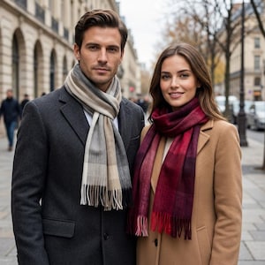 May include: A charcoal gray wool coat paired with a beige, gray, and white plaid scarf featuring fringe ends, alongside a camel-colored wool coat worn with a deep red and burgundy plaid scarf that also features fringe ends.
