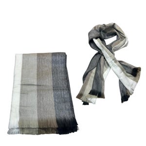 May include: A rectangular throw blanket and a matching scarf featuring a vertical striped pattern in shades of white, beige, light brown, dark gray, and black. Both items have a soft, textured appearance and include fringed edges at the ends.