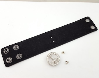 May include: Black leather bracelet with silver studs and a peace sign charm with rhinestones.