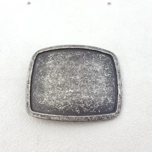 Peut inclure: Une boucle de ceinture argentée avec une finition texturée vieillie. La boucle est rectangulaire et a une surface lisse et plate.