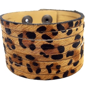 May include: A brown leather cuff bracelet with a leopard print design. The bracelet is made of multiple layers of leather and has a snap closure.