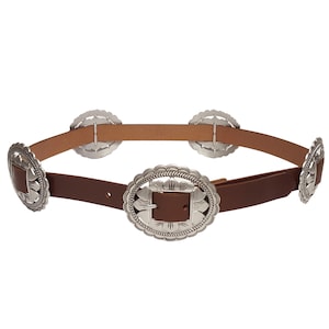 May include: A brown leather belt with silver-colored decorative buckles. The belt has a series of round and oval buckles with intricate designs. The belt is a western-style accessory.