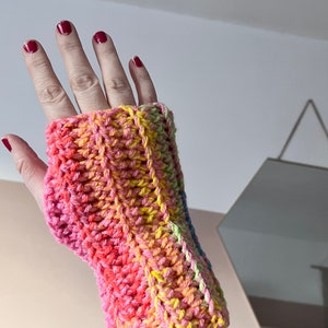 May include: A colorful crocheted fingerless glove with pink, yellow, and green stripes. The glove is made with a textured stitch and has a loose fit.