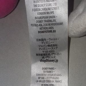 May include: A close-up of a white tag with text from shopDisney.com. The tag includes addresses for the United Kingdom, European Union, Japan, France, and Hong Kong. The tag is partially visible.
