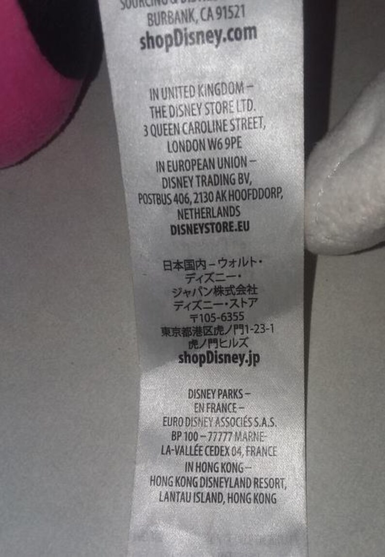 May include: A close-up of a white tag with text from shopDisney.com. The tag includes addresses for the United Kingdom, European Union, Japan, France, and Hong Kong. The tag is partially visible.