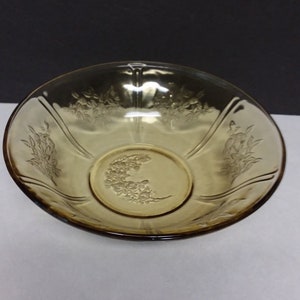 May include: Amber-colored glass bowl with floral etched design. The bowl has a shallow, rounded shape with a wide rim and a decorative floral pattern around the edge and center. The glass is transparent, allowing light to pass through.