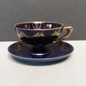 May include: A cobalt blue teacup and saucer set with gold trim and floral designs. The cup has a pedestal base.