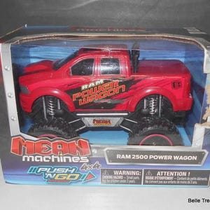 May include: A red RAM 2500 Power Wagon toy truck in a box. The truck has large black tires and the words "RAM POWER WAGON" on the side. The box reads "MEAN machines" and "PUSH N GO!"