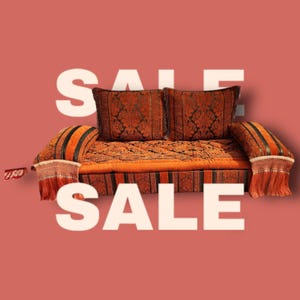 May include: A traditional orange and black patterned sofa with two matching pillows. The sofa has a striped design and fringe trim. The word "SALE" is written in white letters on a red background.