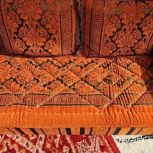 May include: Orange and black patterned couch with a quilted cushion and two matching pillows. The couch has a black and white striped base.