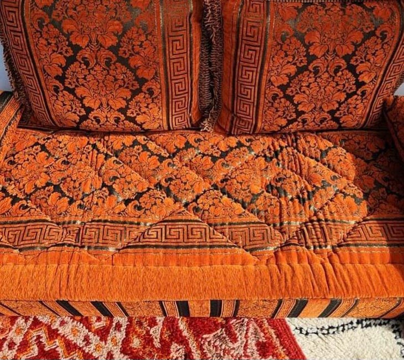 May include: Orange and black patterned couch with a quilted cushion and two matching pillows. The couch has a black and white striped base.