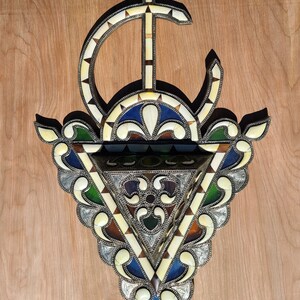 May include: A decorative wall hanging with a triangular shape, featuring intricate metalwork and inlaid ivory and colored glass. The design includes a crescent moon and a star.